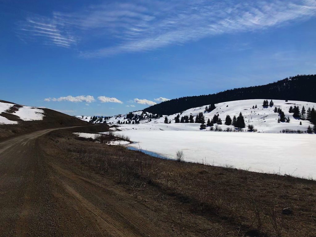 A road leading out of the picture, with a snowy lake on the right side