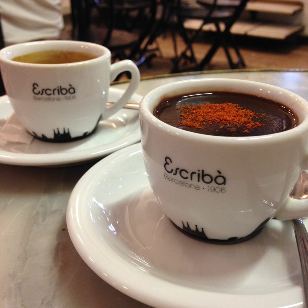 Two white espresso cups in a cafe, one with hot chocolate and the other coffee