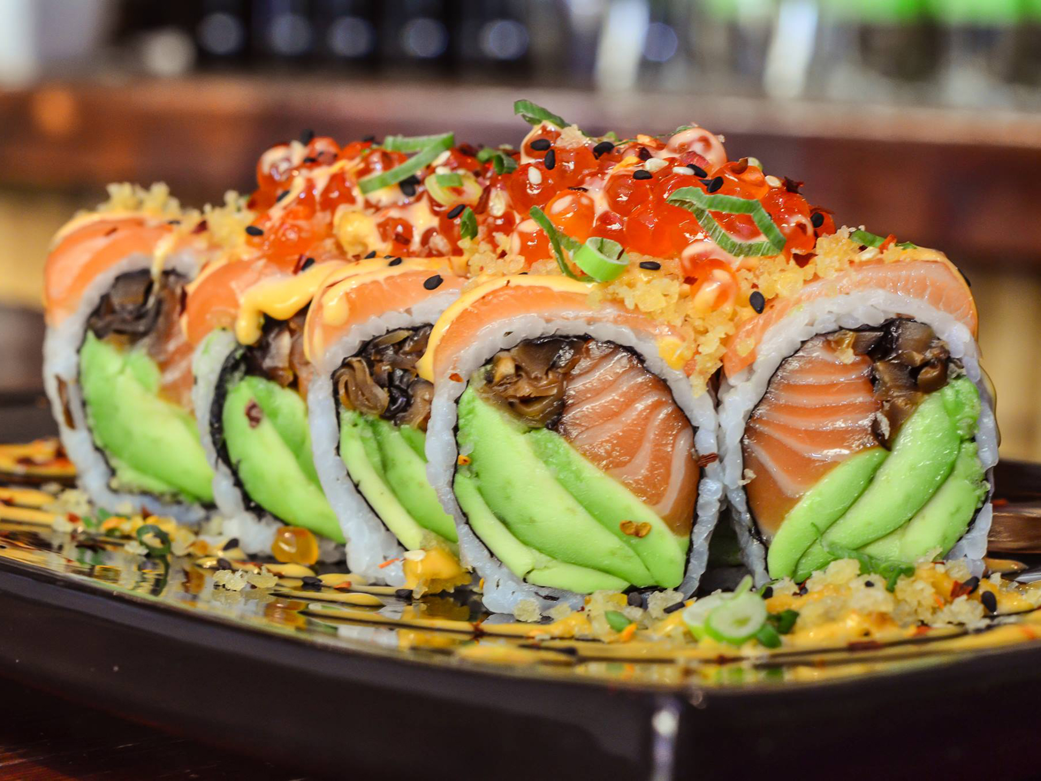 Sushi roll filled with avocado, salmon, and shiitake mushroom, topped with tobiko